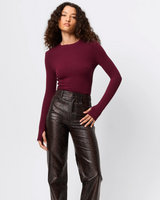 Woman wearing a burgundy long-sleeve top and black leather pants on a white background