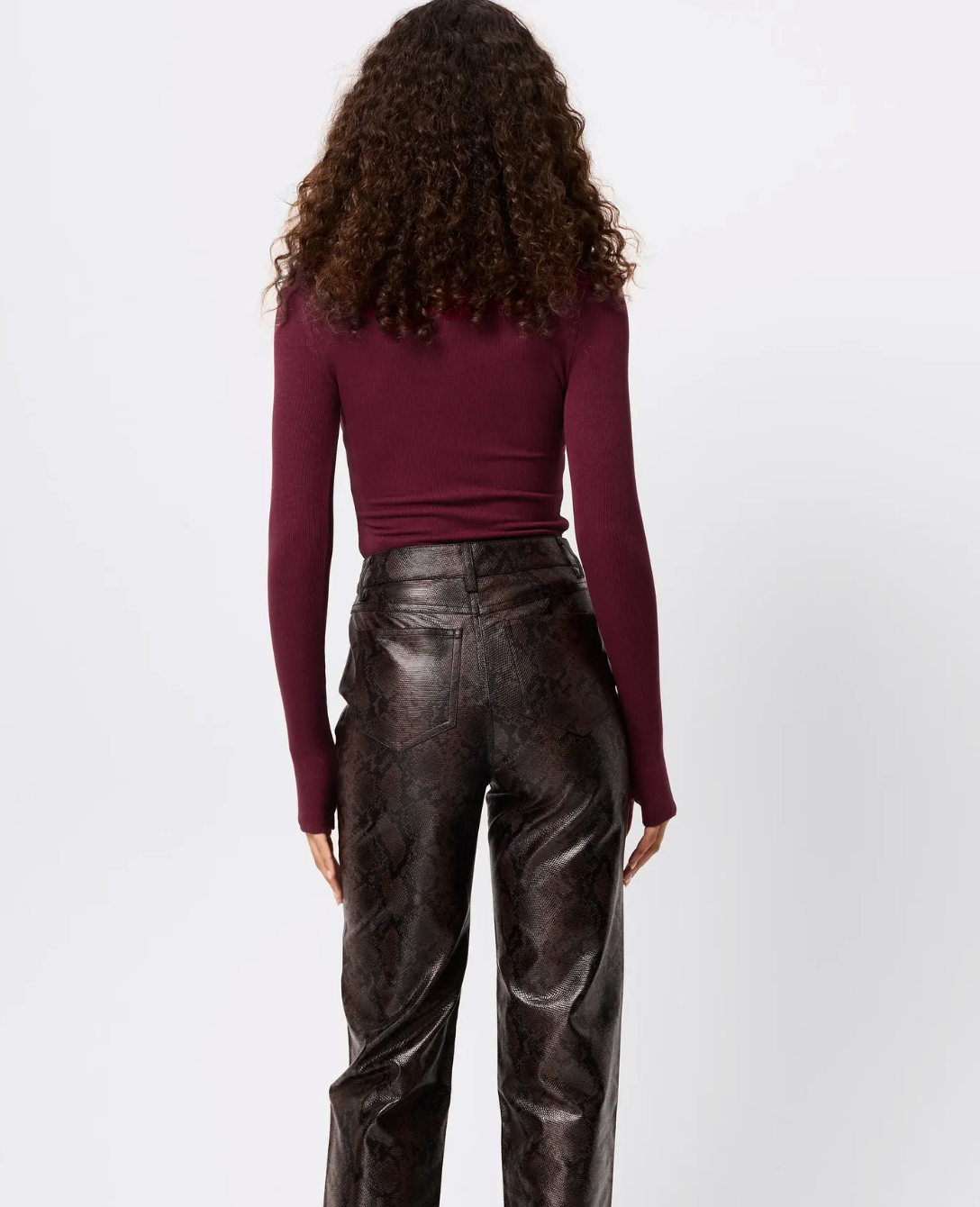 Person wearing a burgundy long-sleeve top and black leather pants on a white background
