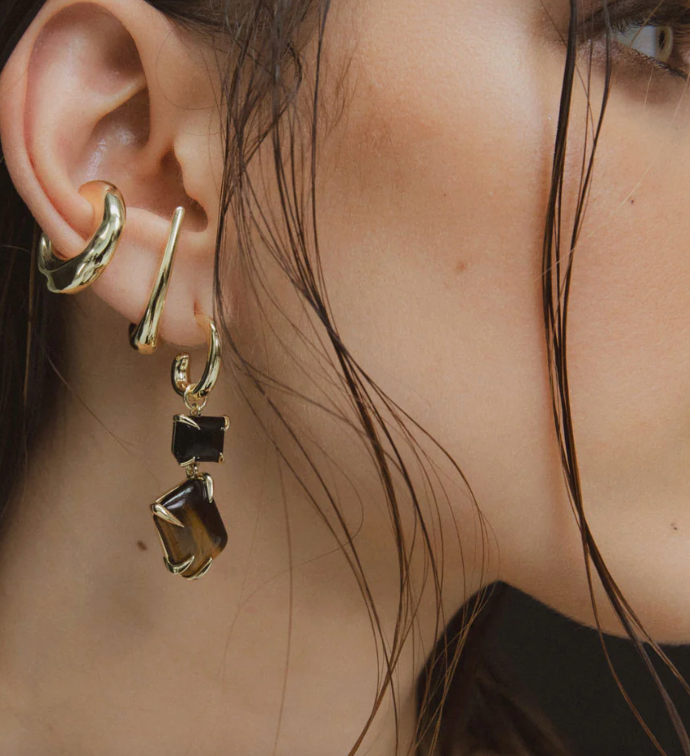 Close-up of a person wearing gold hoop earrings with black stones.