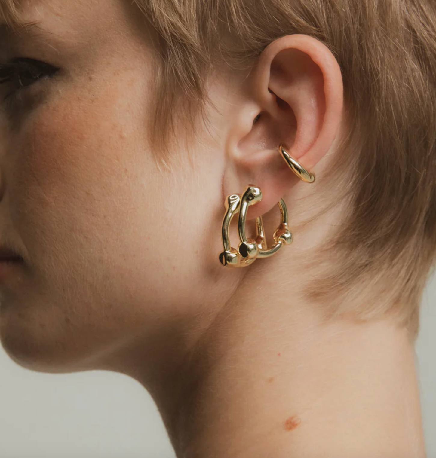 Close-up of a person wearing gold hoop earrings with a neutral background