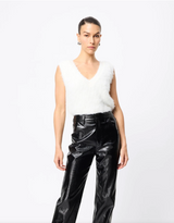 Woman wearing a white sleeveless top and black shiny pants on a white background