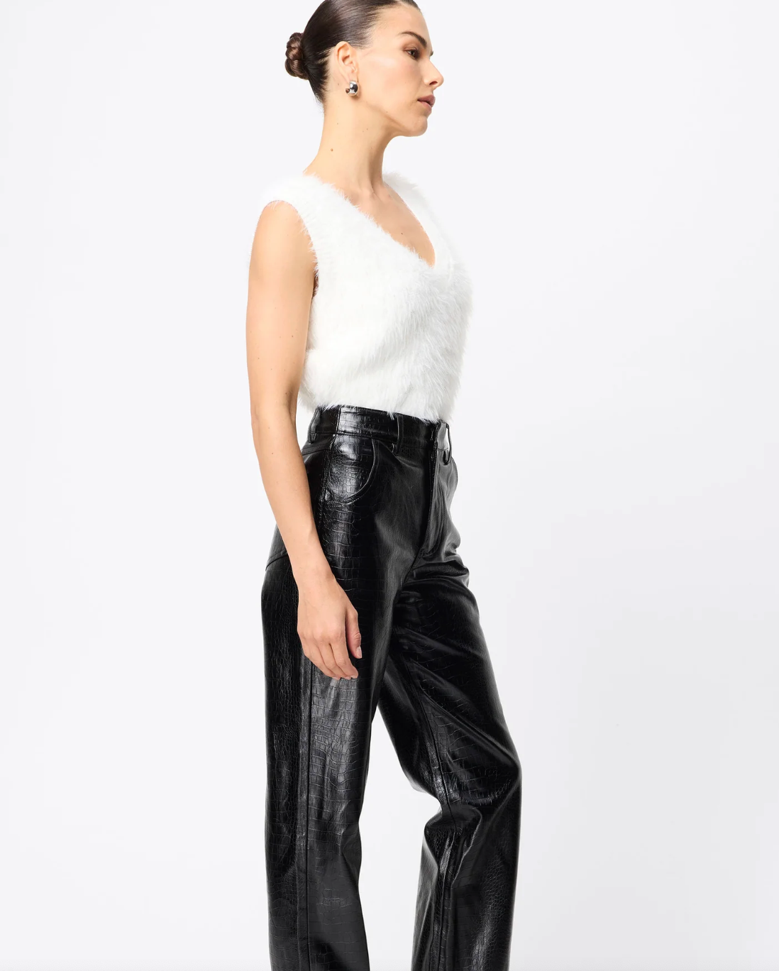 Woman wearing a white sleeveless top and black leather pants on a white background