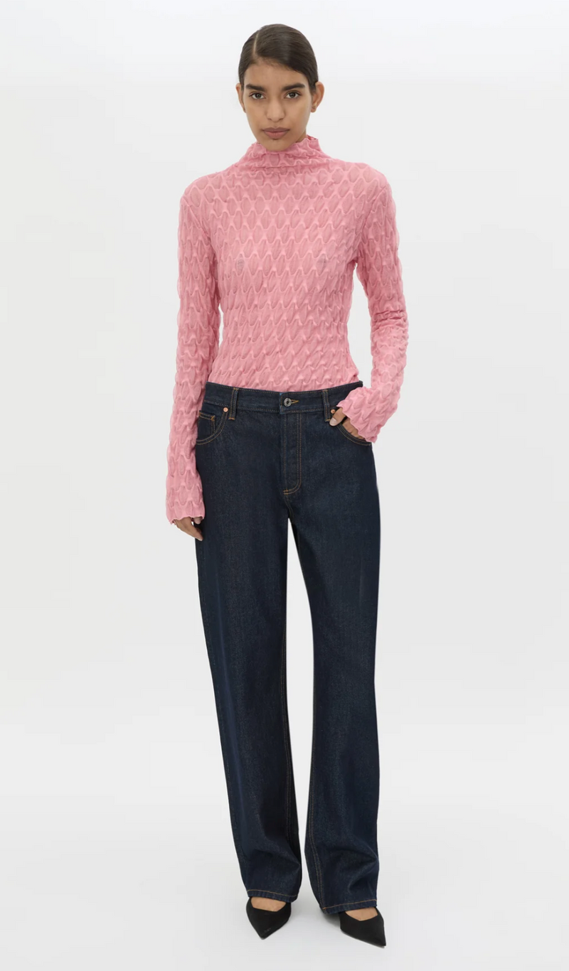 Woman wearing a pink textured sweater and dark blue jeans on a white background