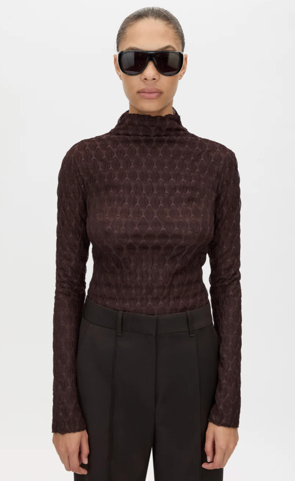 Person wearing a patterned brown long-sleeve top and black pants on a white background