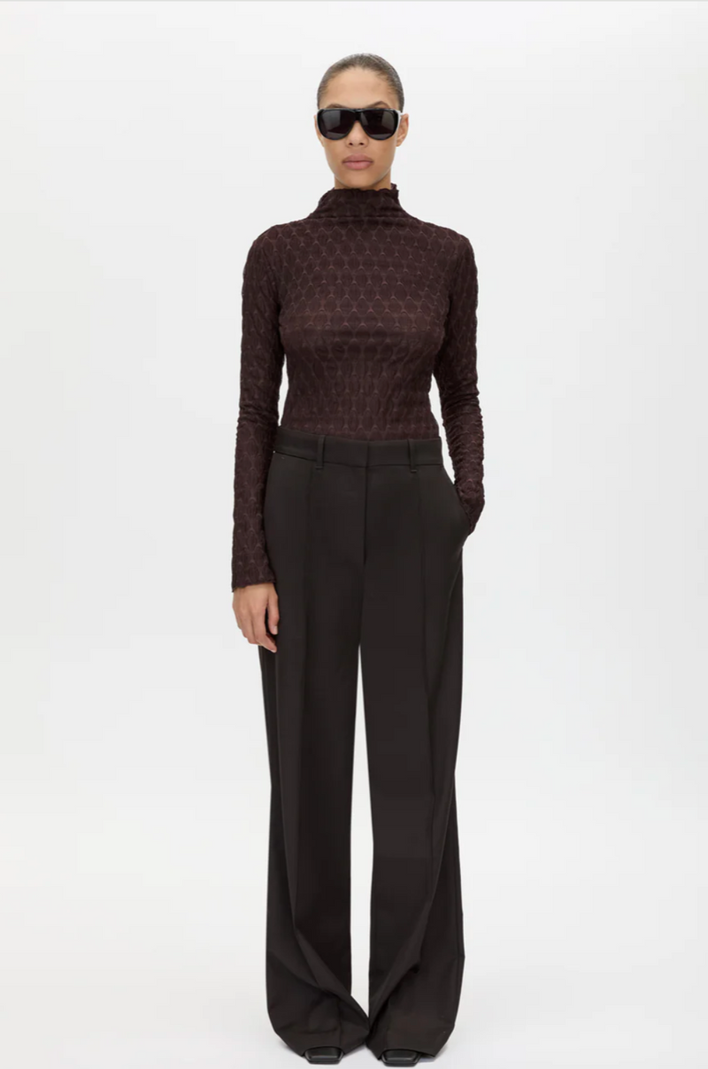 Person wearing a brown patterned turtleneck and black wide-leg pants on a white background