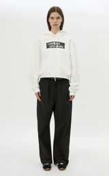 Person wearing a white hoodie with a logo and black pants on a white background