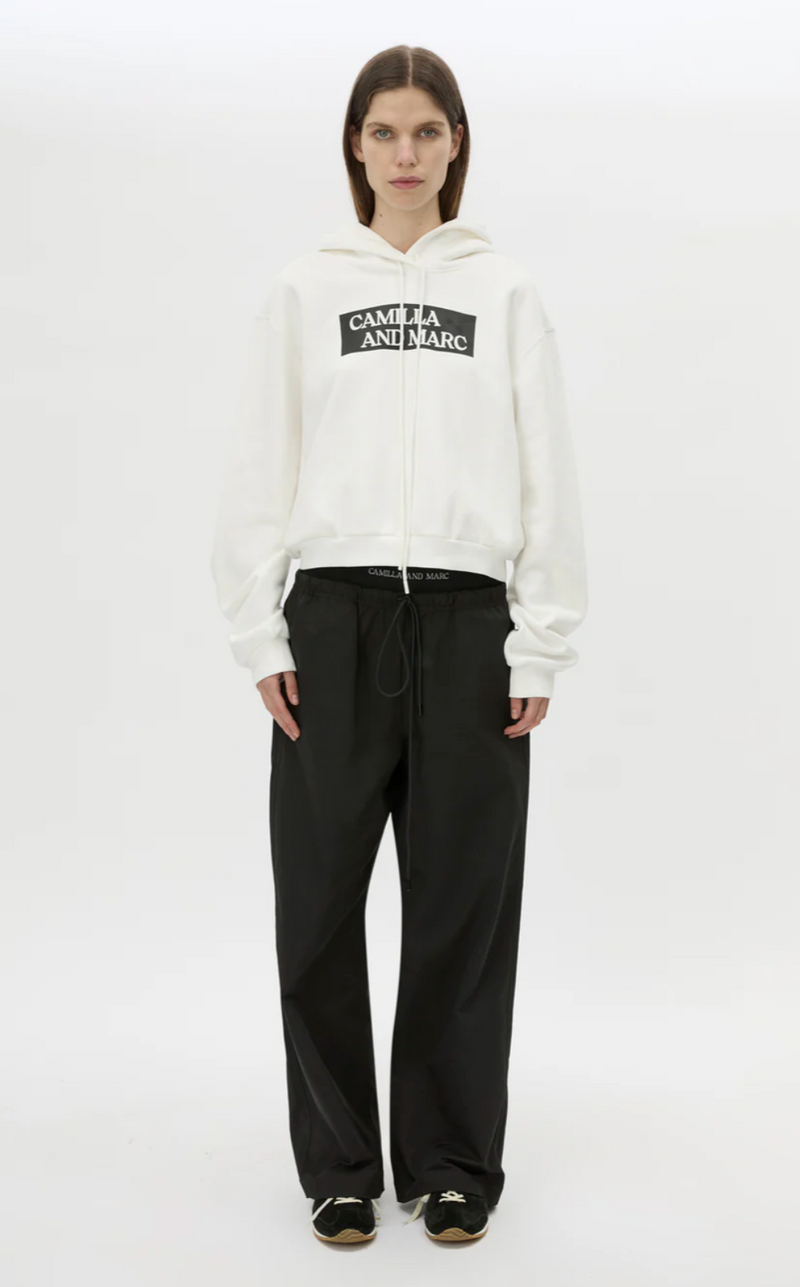 Person wearing a white hoodie with a logo and black pants on a white background