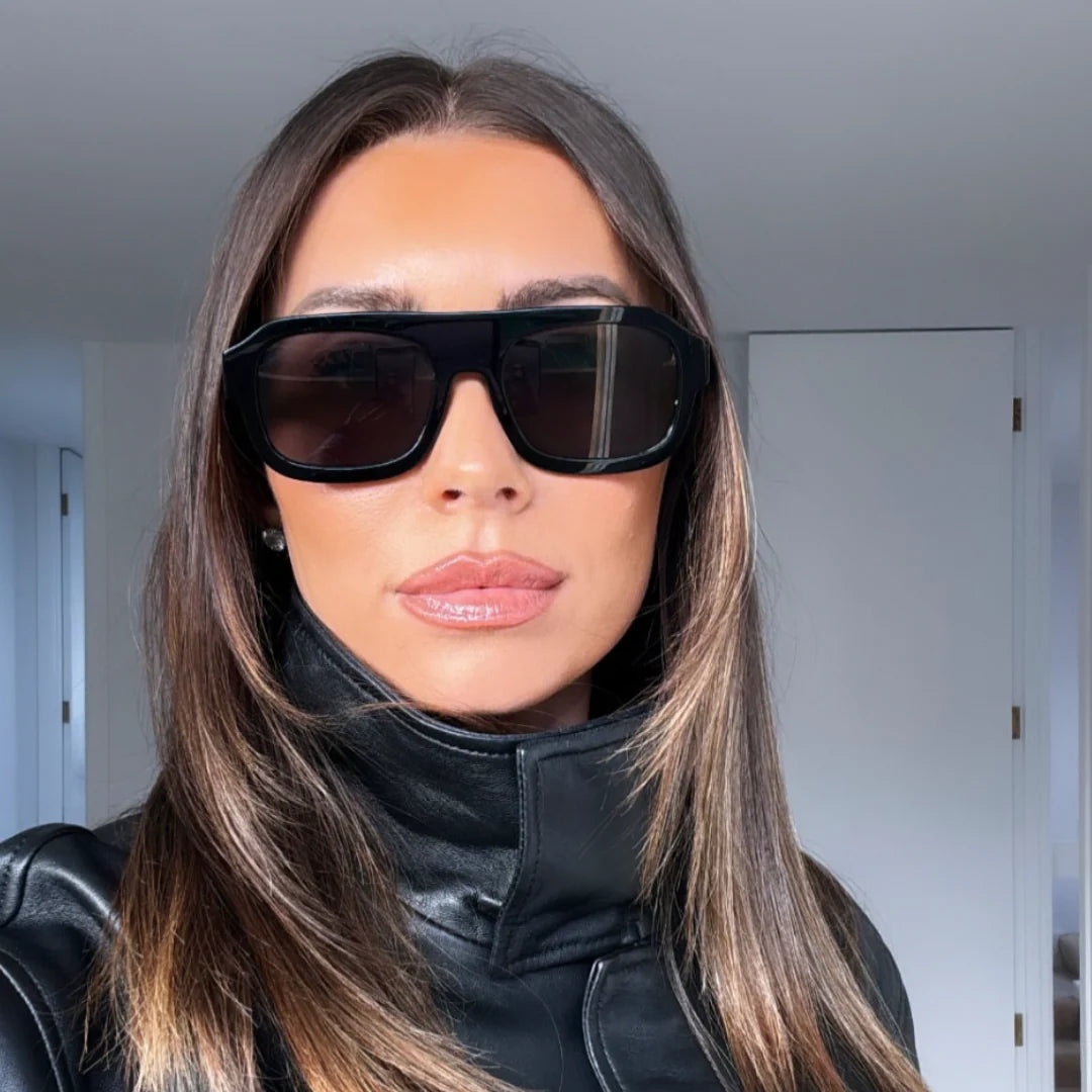 Woman wearing black sunglasses and a black outfit indoors.