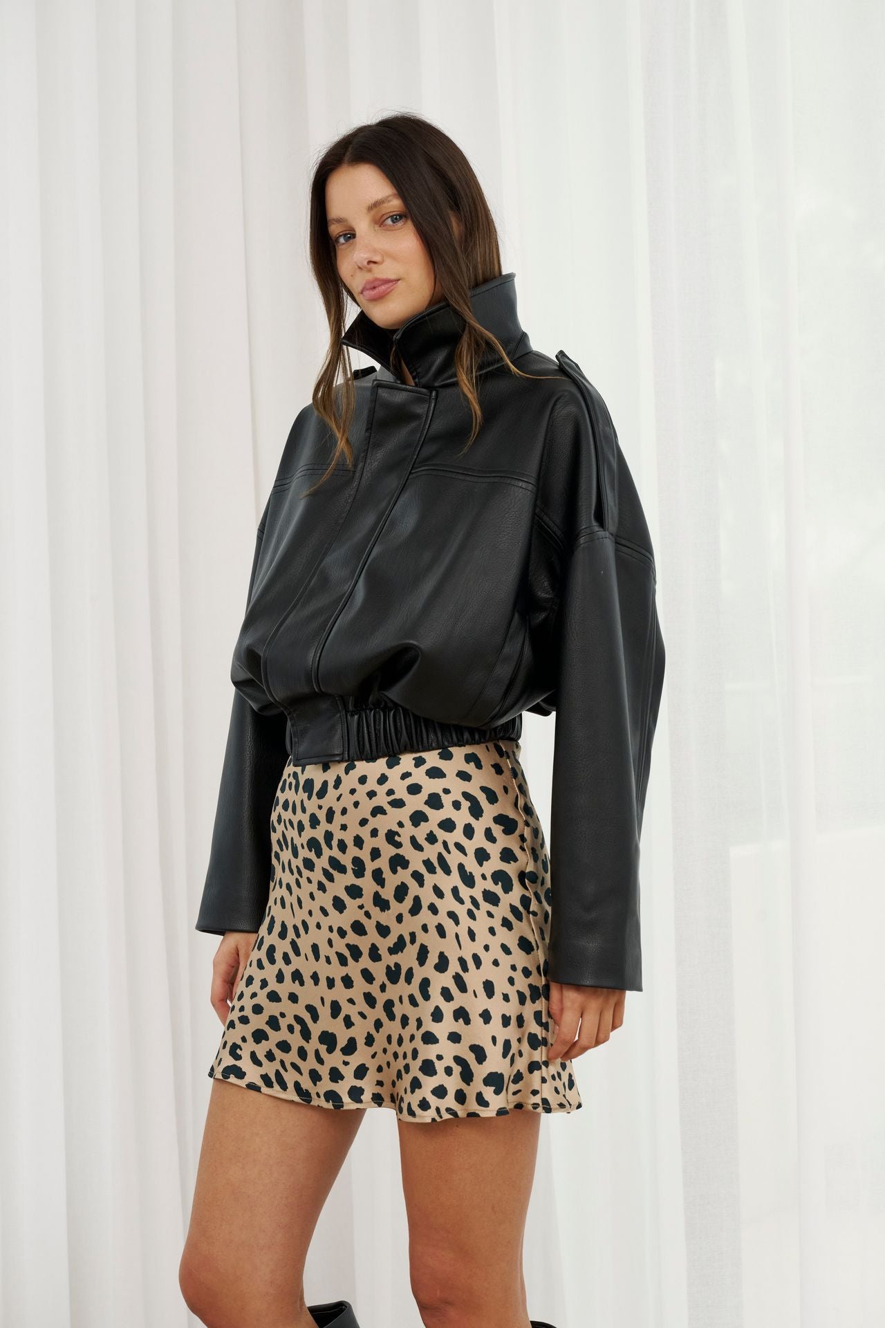 Woman wearing a black jacket and leopard print shorts against a white curtain background