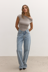 Woman wearing a beige top and light blue jeans against a white background
