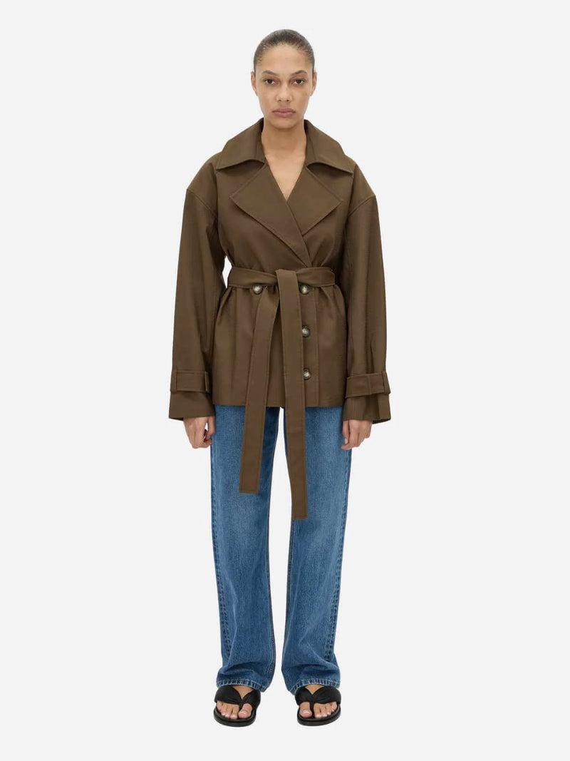 Person wearing a brown trench coat and blue jeans on a white background
