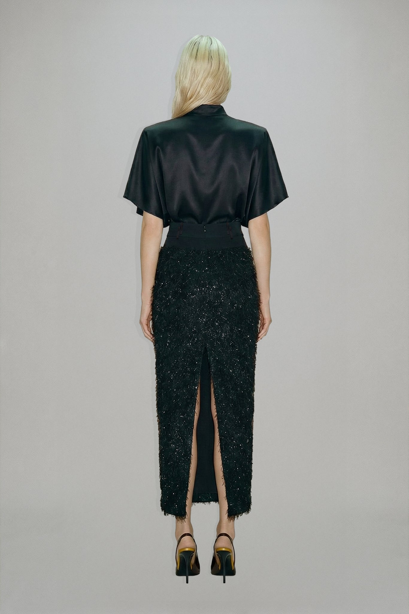 Person wearing a black outfit with a high slit on a plain background